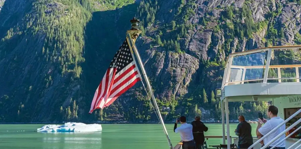 Photo of an American flag waving on a ship deck with a rocky mountain backdrop