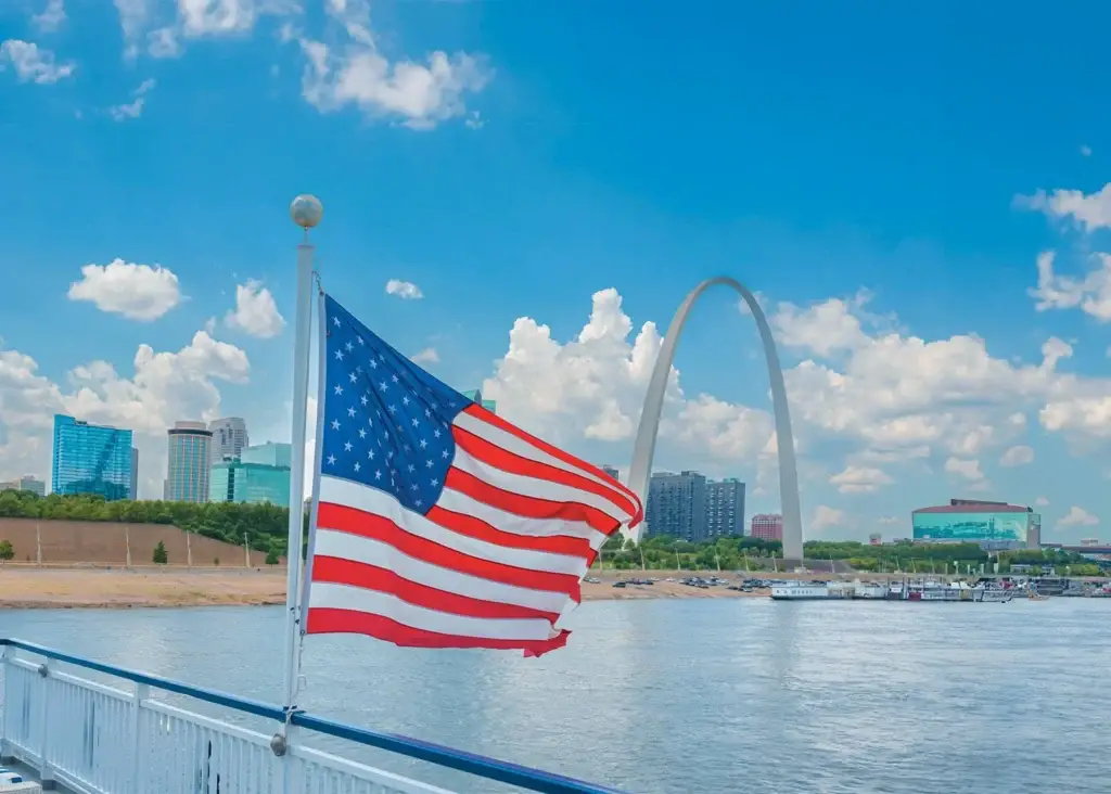 Photo of American flag waving from deck railing near St Louis Gateway Arch waterfront