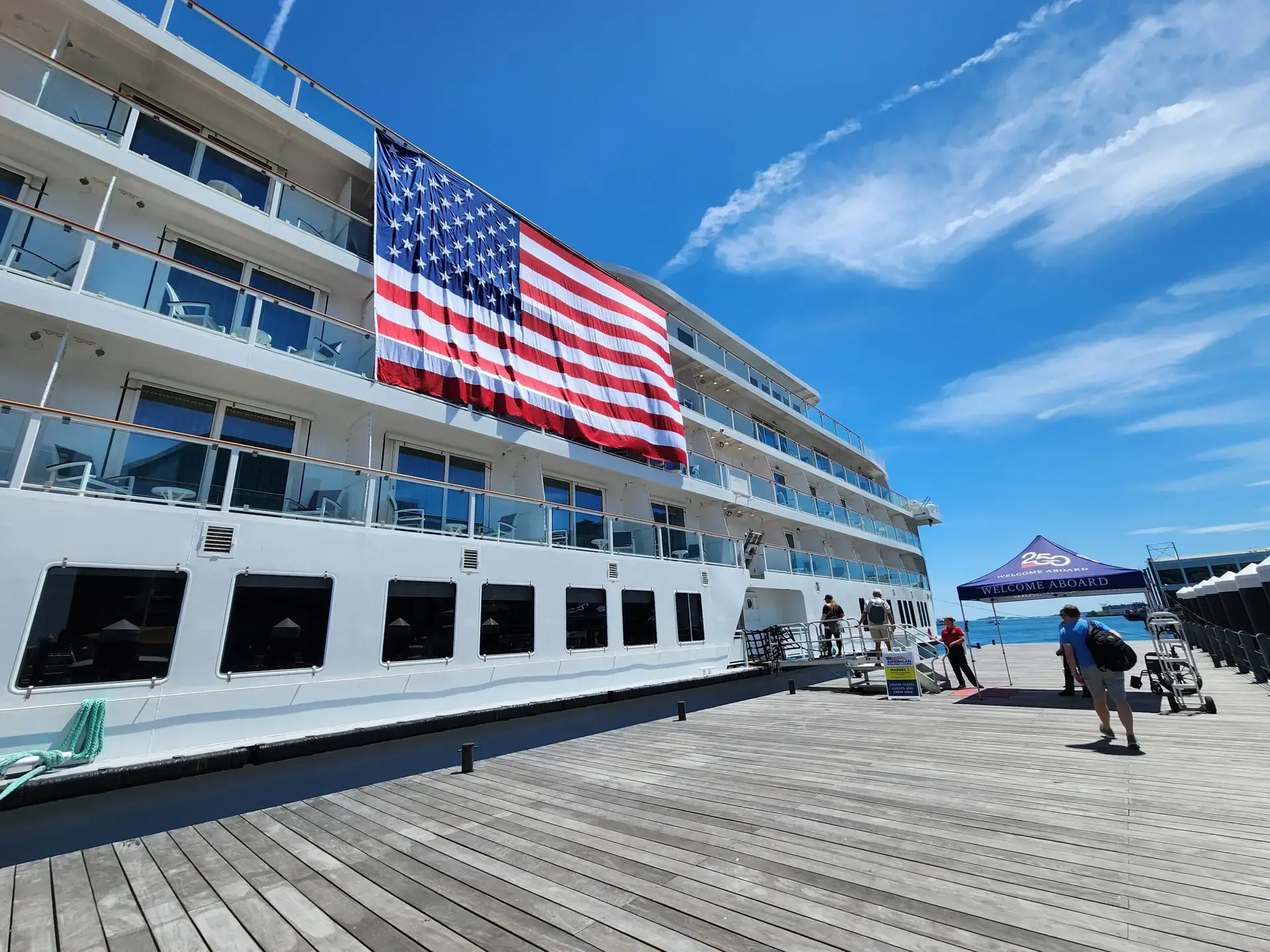 Photo of a large cruise ship docked at a wooden pier displaying a giant American flag