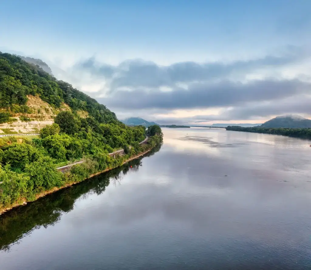 Photo of a wide calm river lined with forested hills under a cloudy morning sky