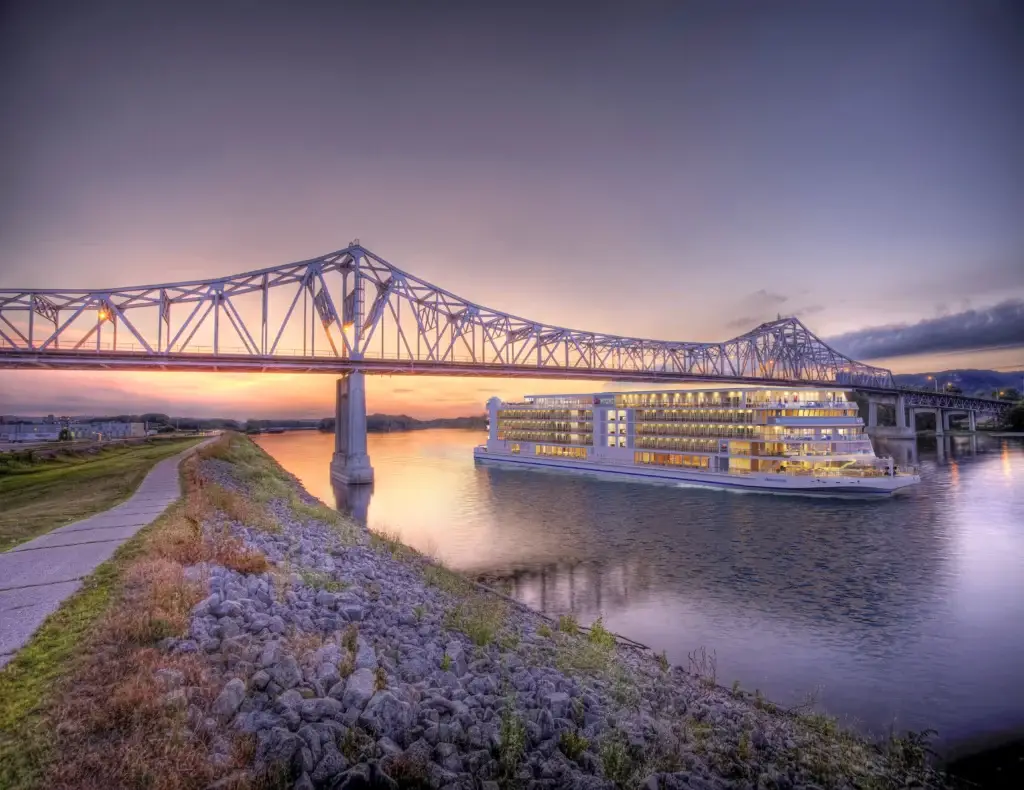 Photo-of-illuminated-Viking-river-ship-passing-under-bridge-at-sunset