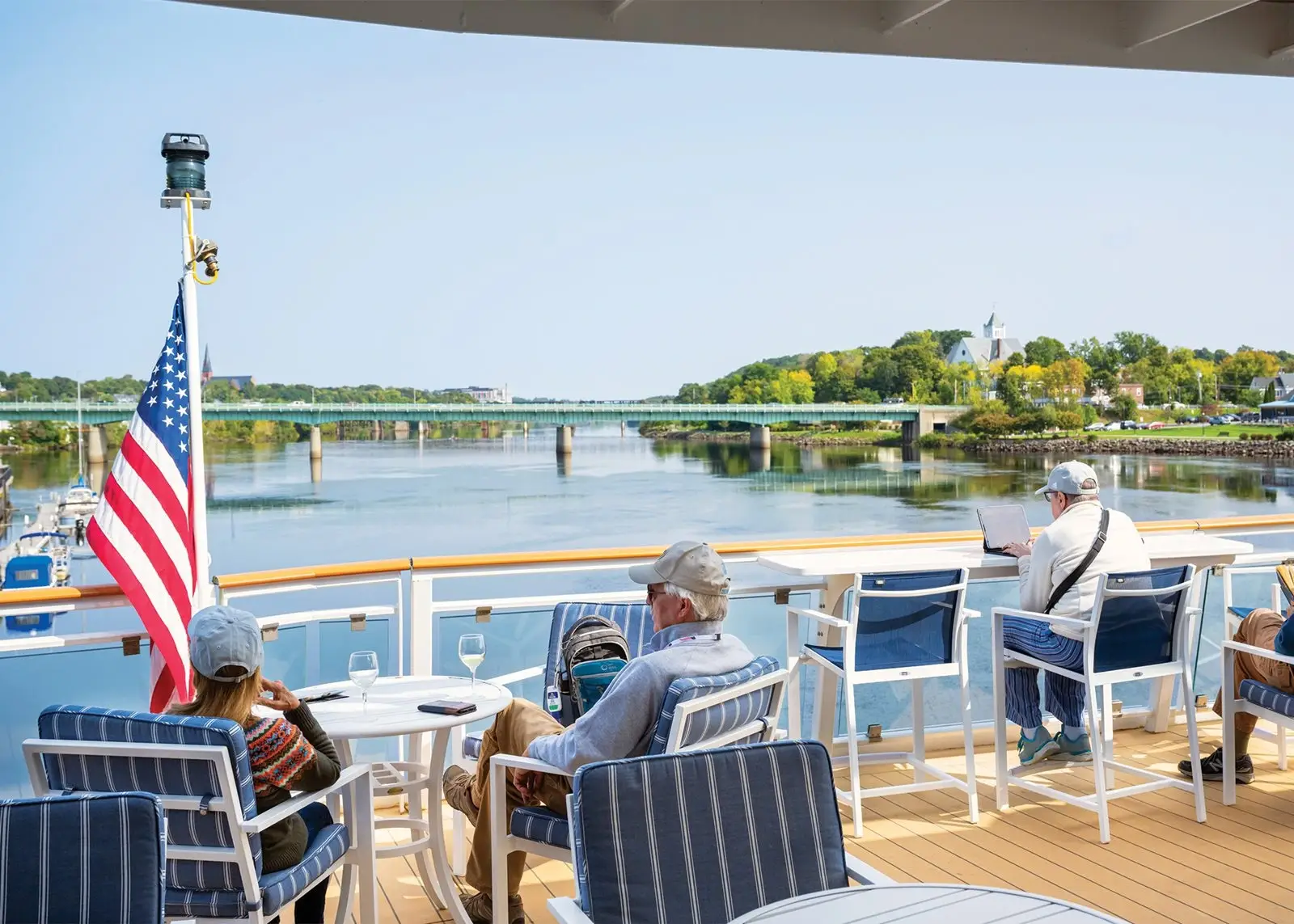 Photo of passengers relaxing on outdoor observation deck of cruise ship by river