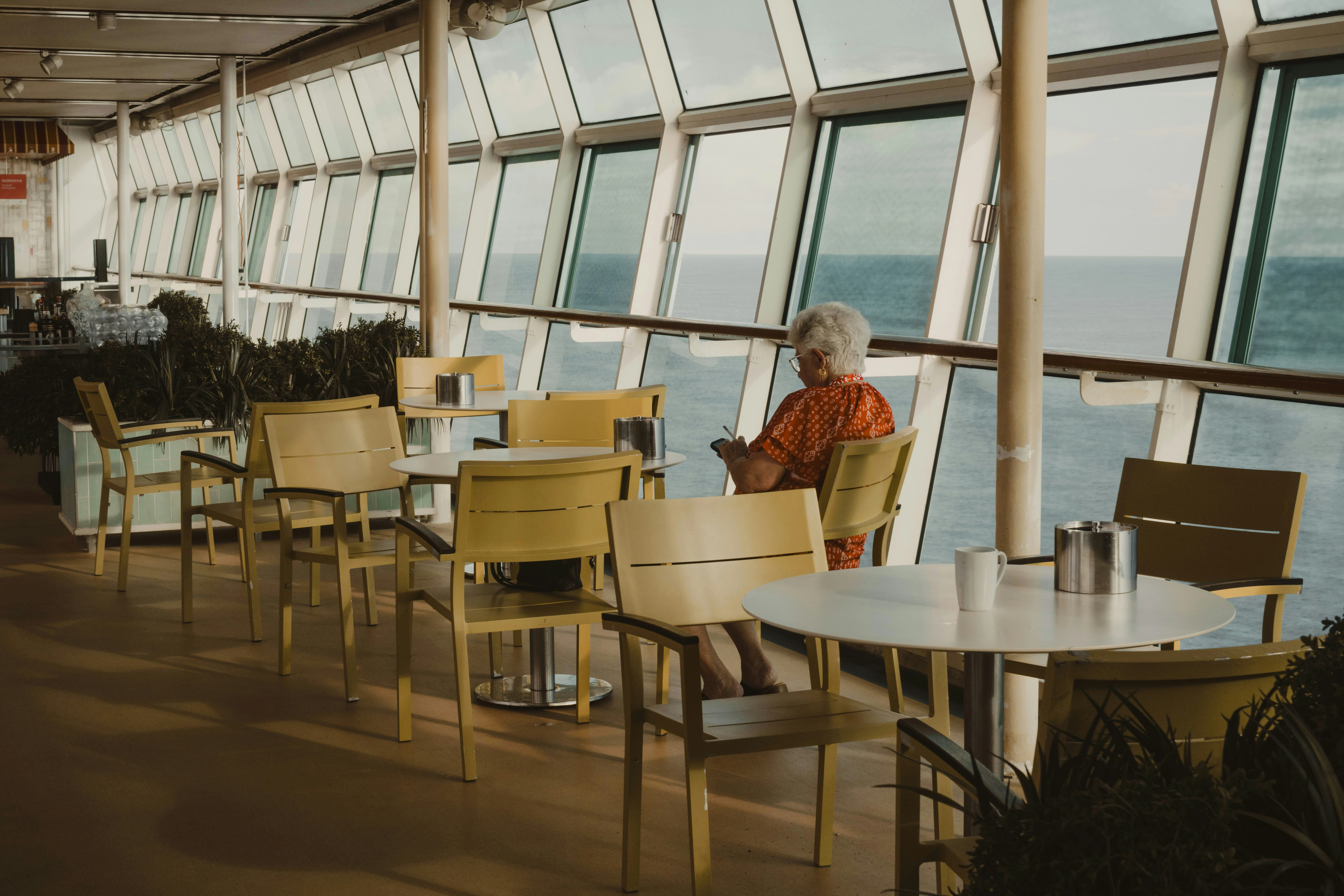 Photo of senior woman sitting in cruise ship lounge near large ocean view windows