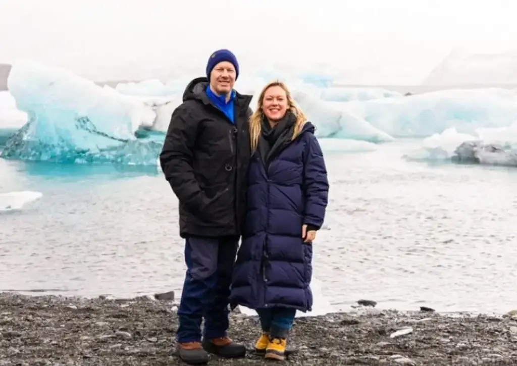 Photo-of-smiling-couple-in-winter-parkas-standing-in-front-of-icy-glacier-lagoon