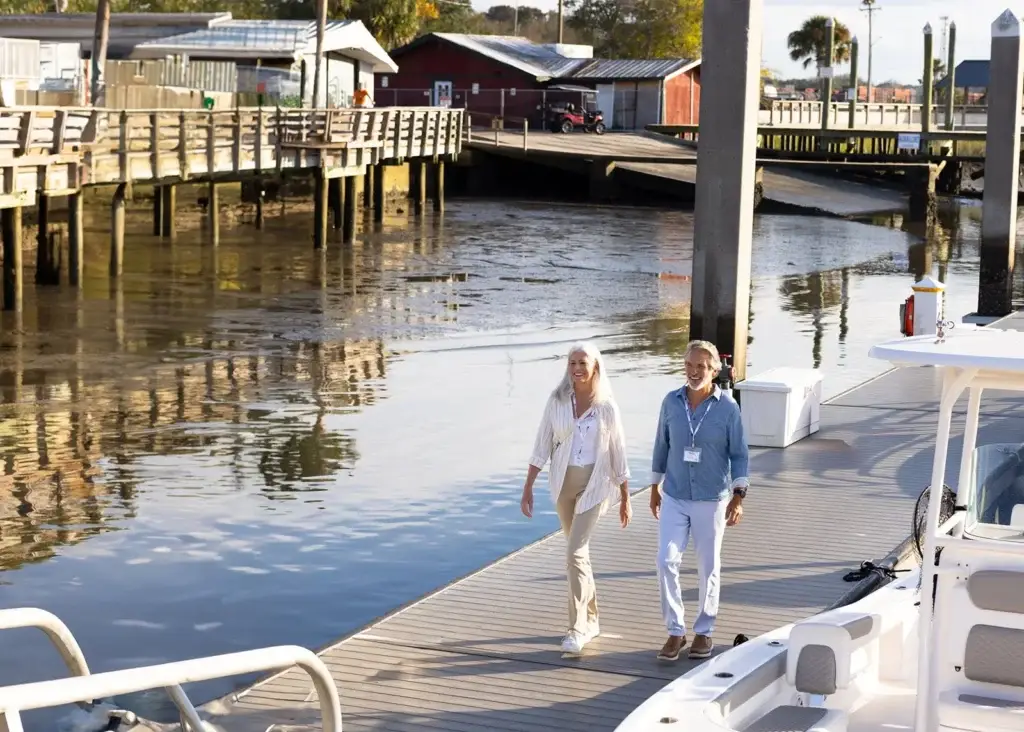 Photo of a smiling senior couple walking on wooden pier dock near water