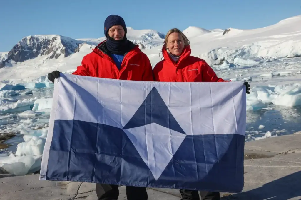 Photo of travelers holding Antarctic flag on ice expedition featured in how much does it cost to go to Antarctica