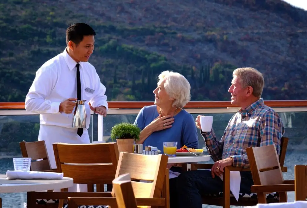 Photo of a Viking ocean cruise waiter serving guests dining outdoors on the Aquavit Terrace